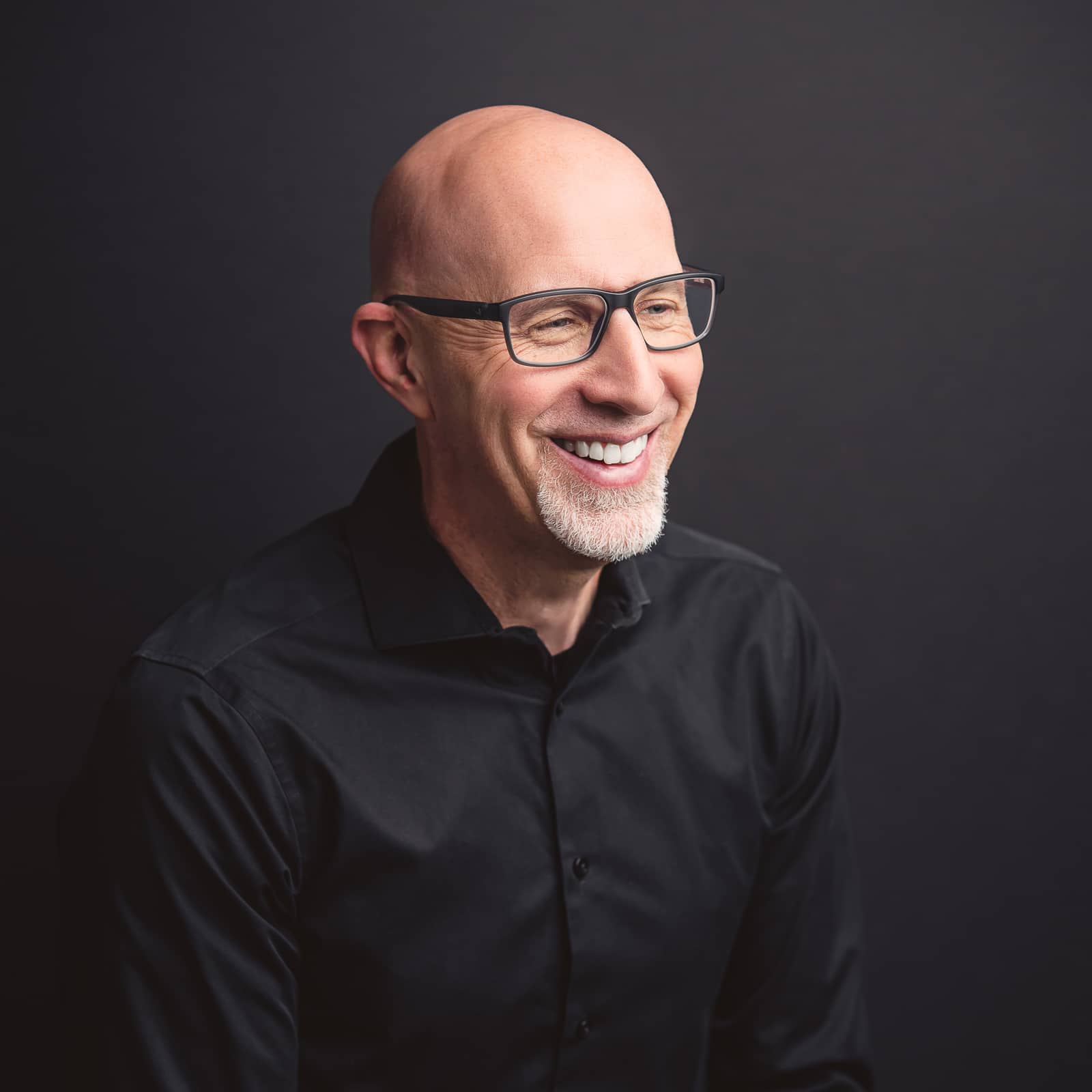 Jason Shupp Smiling bald man, glasses, smiling in studio, black shirt