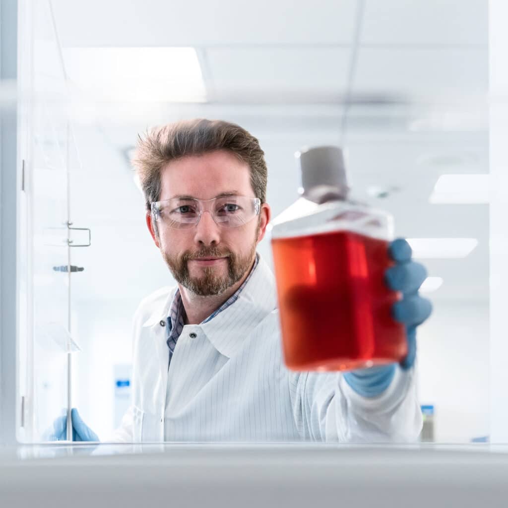Scientist in lab holding red liquid in sealed bottle.