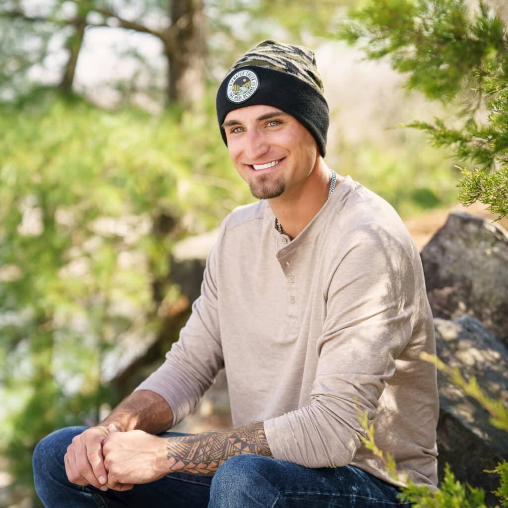 smiling man wearing knit cap, seated in sunny outdoors